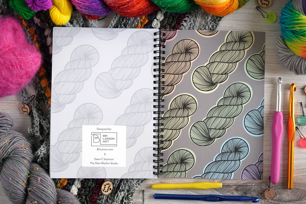 Crochet project journal for patterns by Bri Larson Art featuring yarn designs and surrounded by colorful yarn and crochet hooks