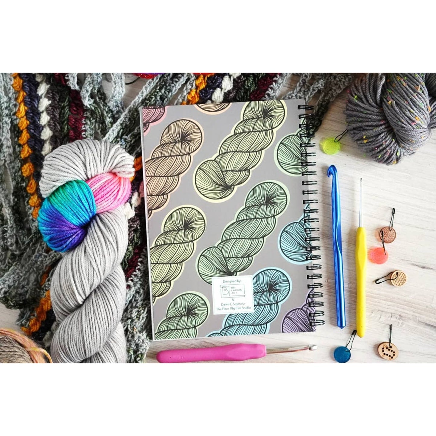 Crochet project journal for patterns with yarn skeins and crochet hooks laid on a wooden table