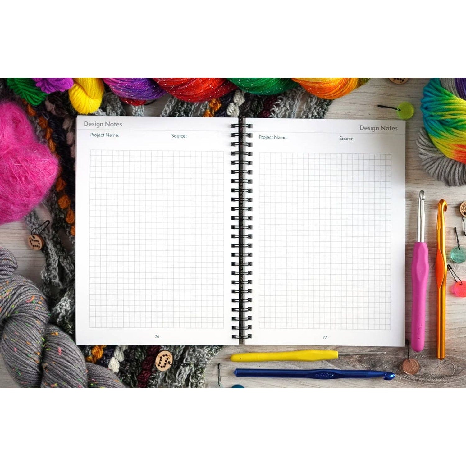 Open crochet project journal for patterns surrounded by colorful yarn and crochet hooks on wooden table
