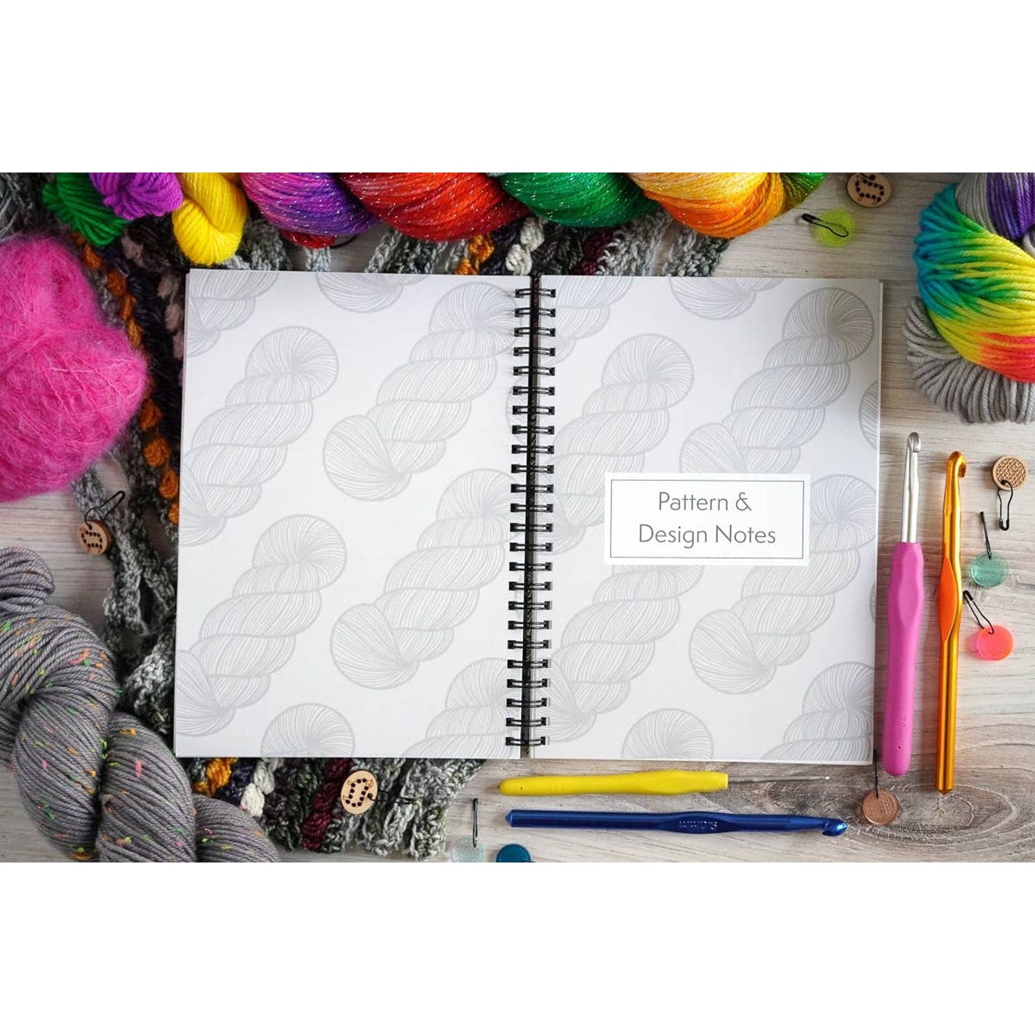 Open crochet project journal for patterns showing pattern and design notes surrounded by colorful yarn and crochet hooks