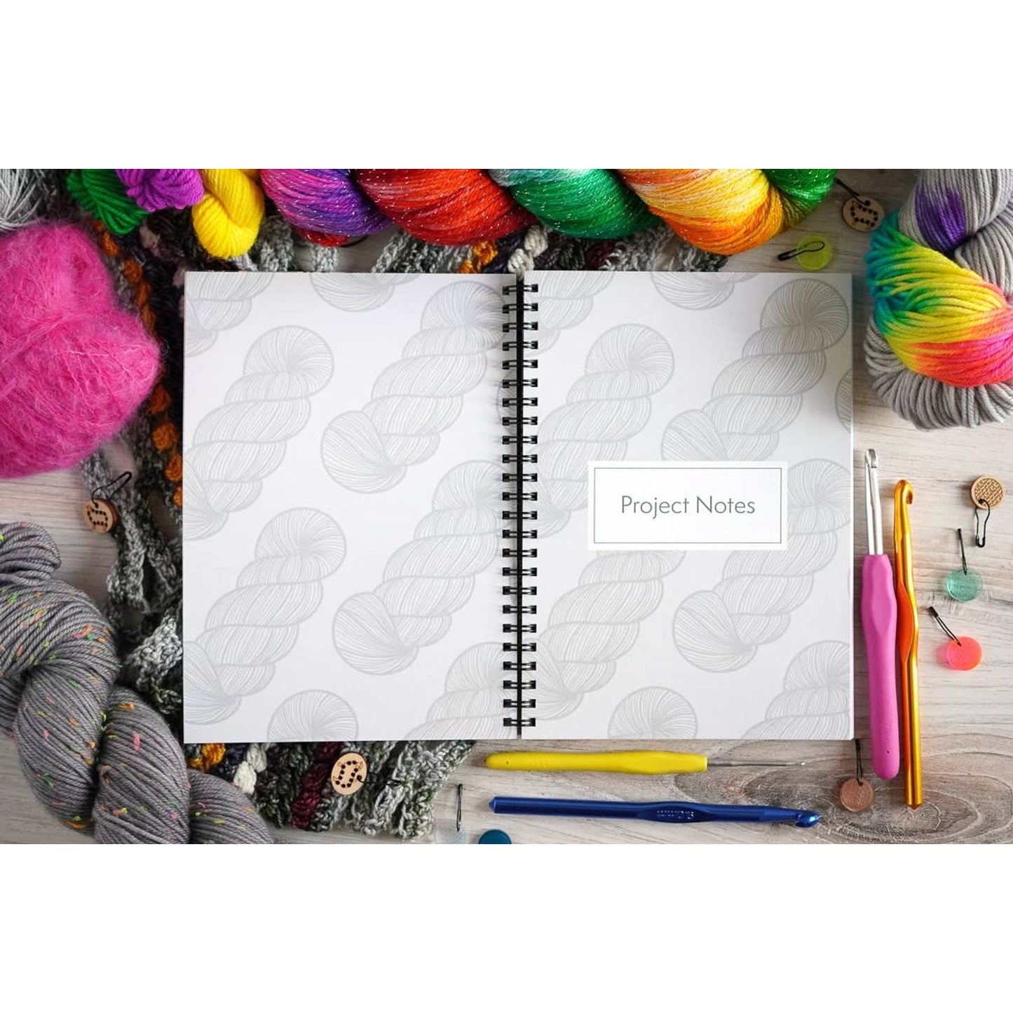 Open crochet project journal for patterns surrounded by colorful yarn and crochet hooks by Bri Larson Art