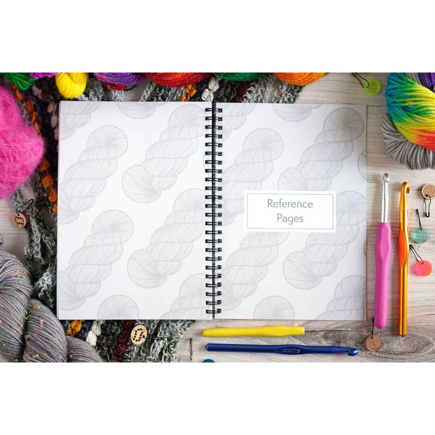 Open crochet project journal for patterns surrounded by colorful yarn and crochet hooks on a wooden table