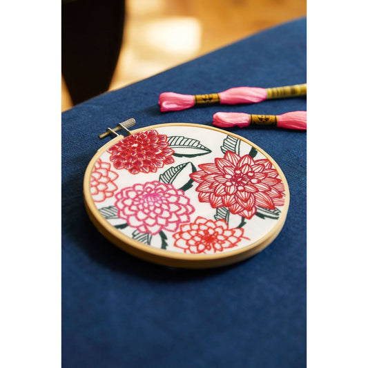 DMC embroidery hoop featuring bright red and pink dahlias design with embroidery floss beside it