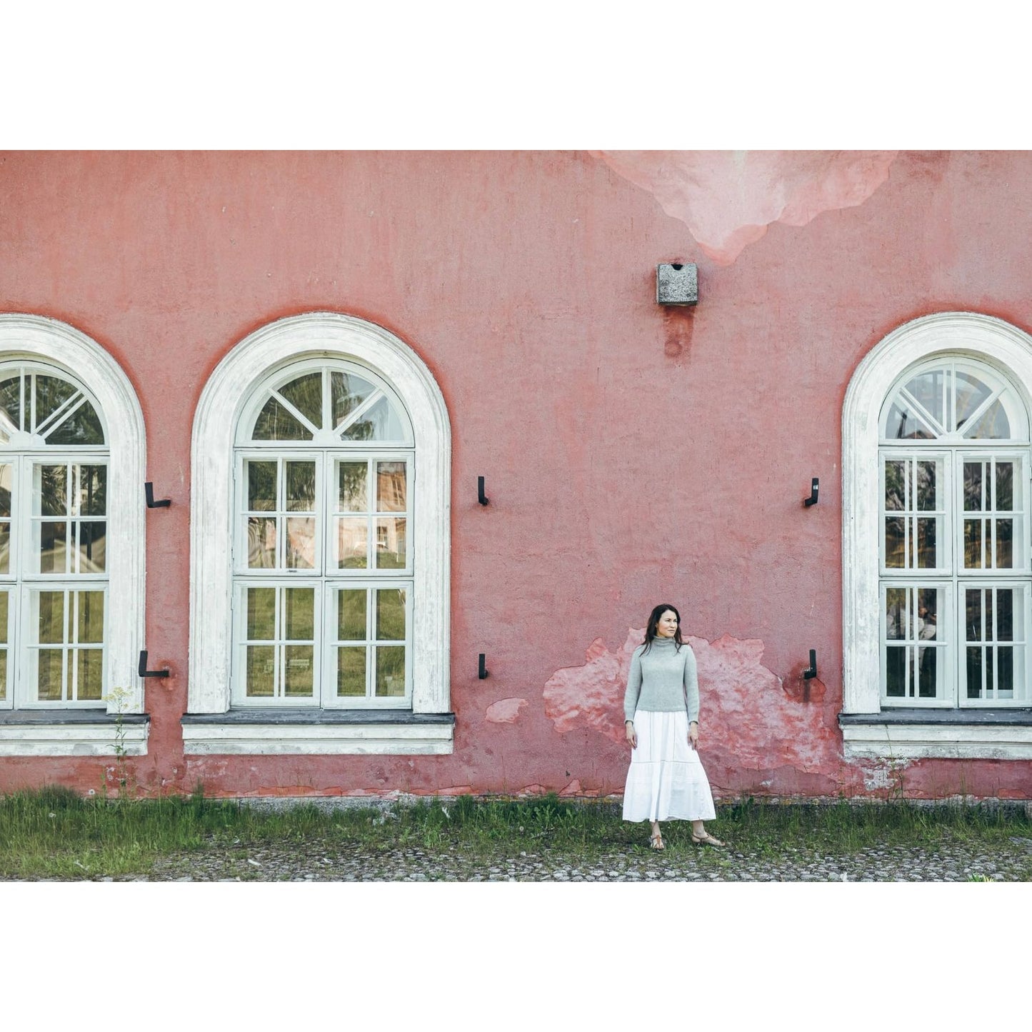 Woman in a cozy sweater and white skirt standing by vintage windows, demonstrating how to knitwear style