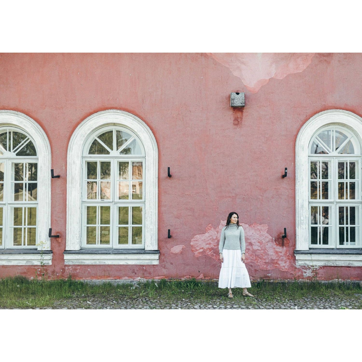 Woman in a cozy sweater and white skirt standing by vintage windows, demonstrating how to knitwear style