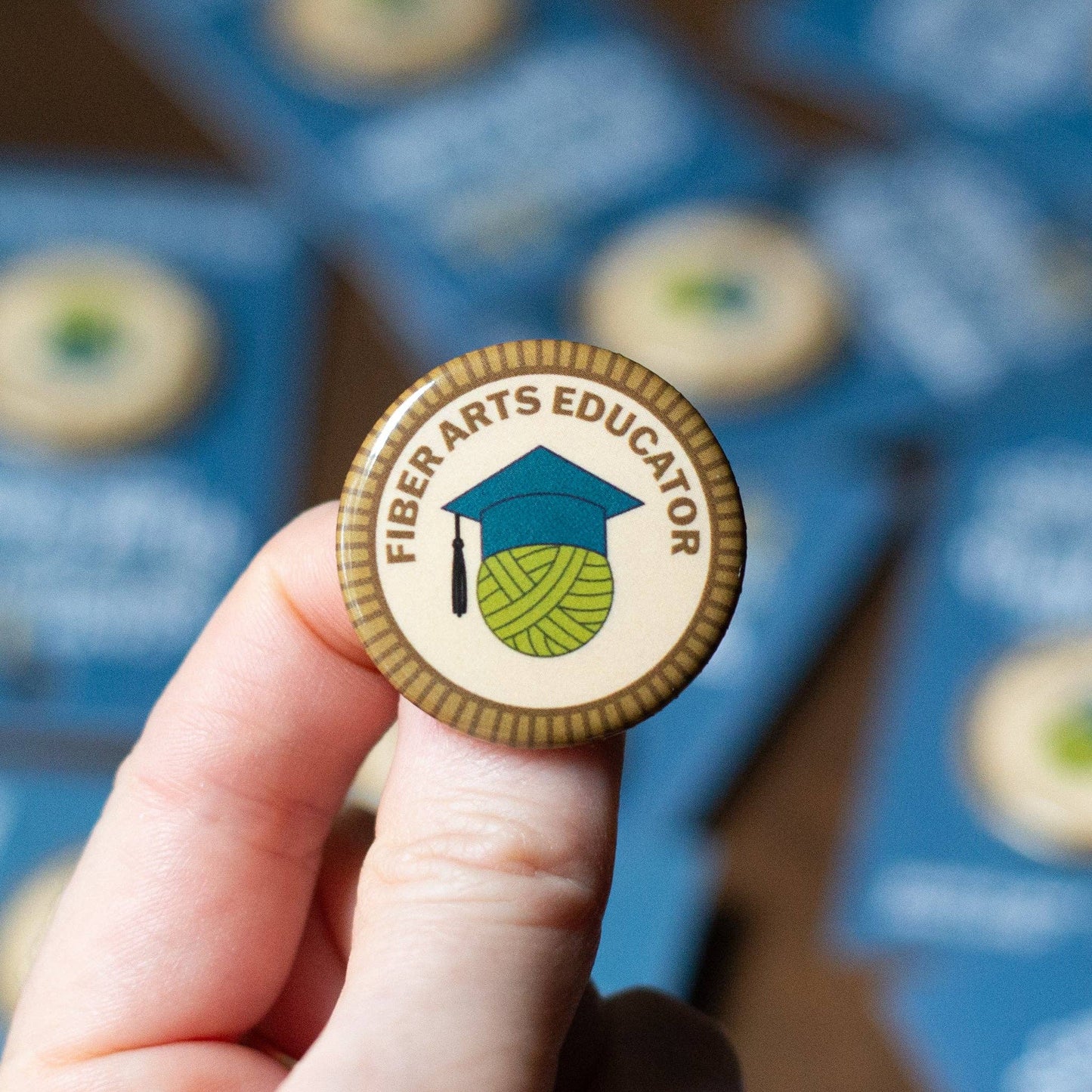 Camp Stitchwood Fiber Arts Educator Button Featuring Yarn and Graduation Cap Design