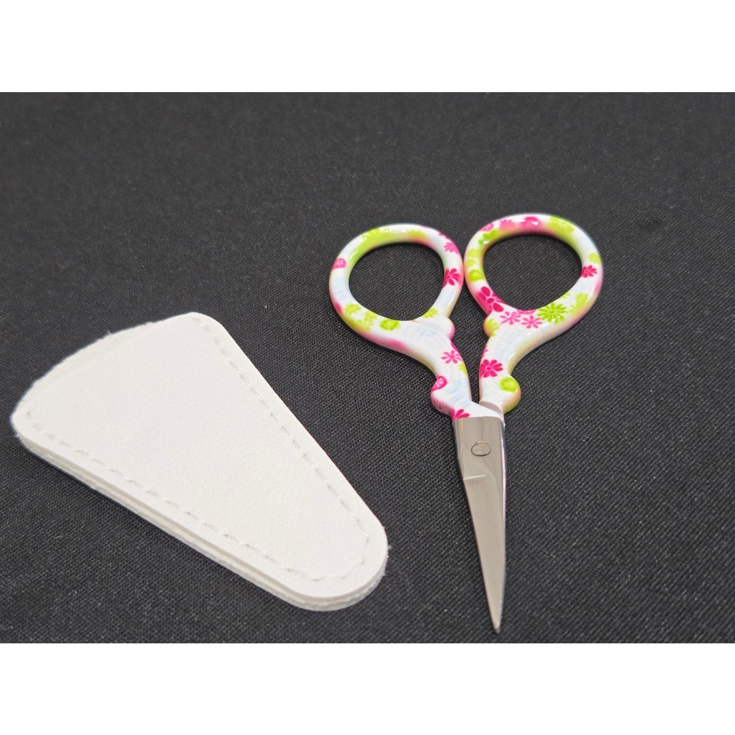 Amazon embroidery scissors with floral patterned handles and white protective case on black background