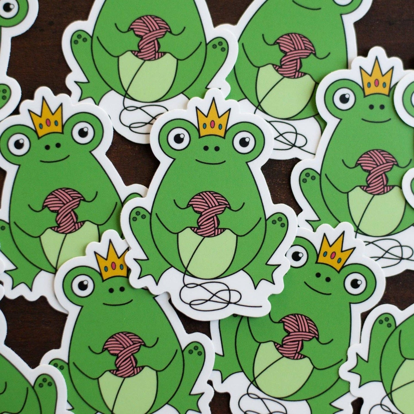 Colorful frog sticker featuring a frog with a crown holding yarn in its hands