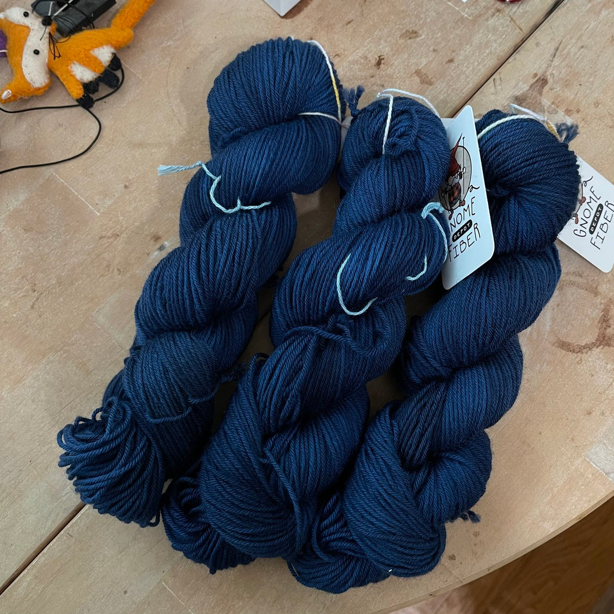 Three skeins of dark blue Gnome Depot Fiber DK weight yarn arranged on a table