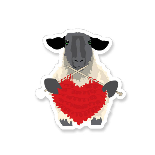 sheep knitting vinyl sticker of a black faced sheep knitting a red heart with wooden needles