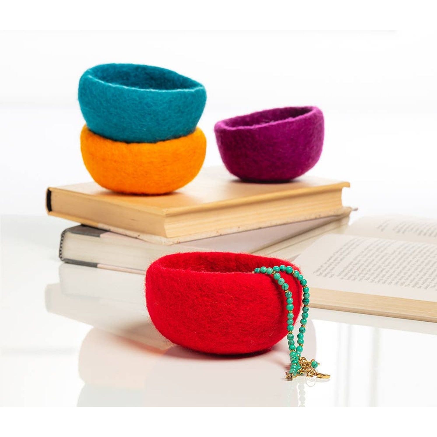 Colorful handmade yarn storage bowls in red, orange, blue, and purple arranged on books