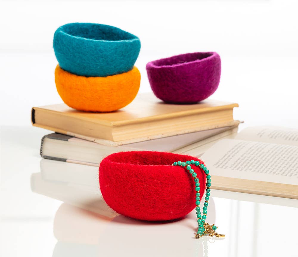 Colorful handmade yarn storage bowls in red, orange, blue, and purple arranged on books
