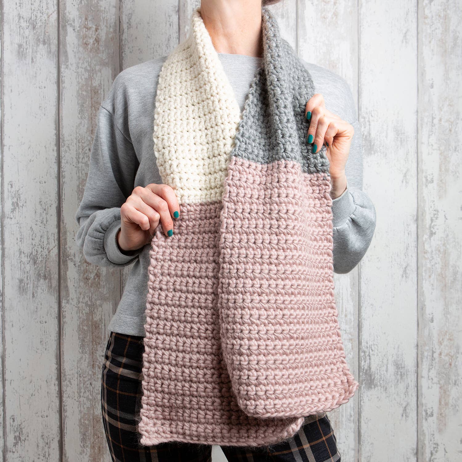 Model wearing chunky colorblock scarf in cream gray and blush, hands holding scarf, Hannah's crochet kit for beginners