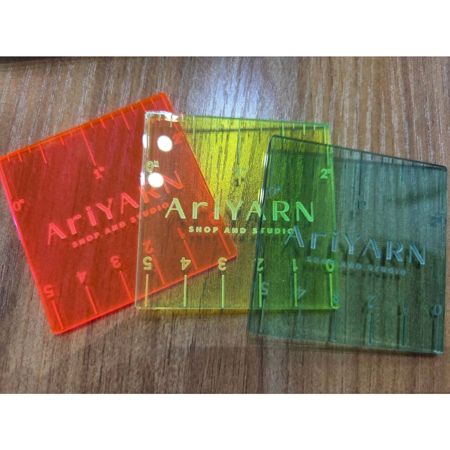 Colorful HapBee AriYARN ruler for knitting in red, yellow, and green translucent plastic on wooden surface
