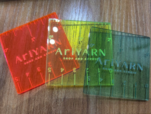 Colorful HapBee AriYARN ruler for knitting in red, yellow, and green translucent plastic on wooden surface