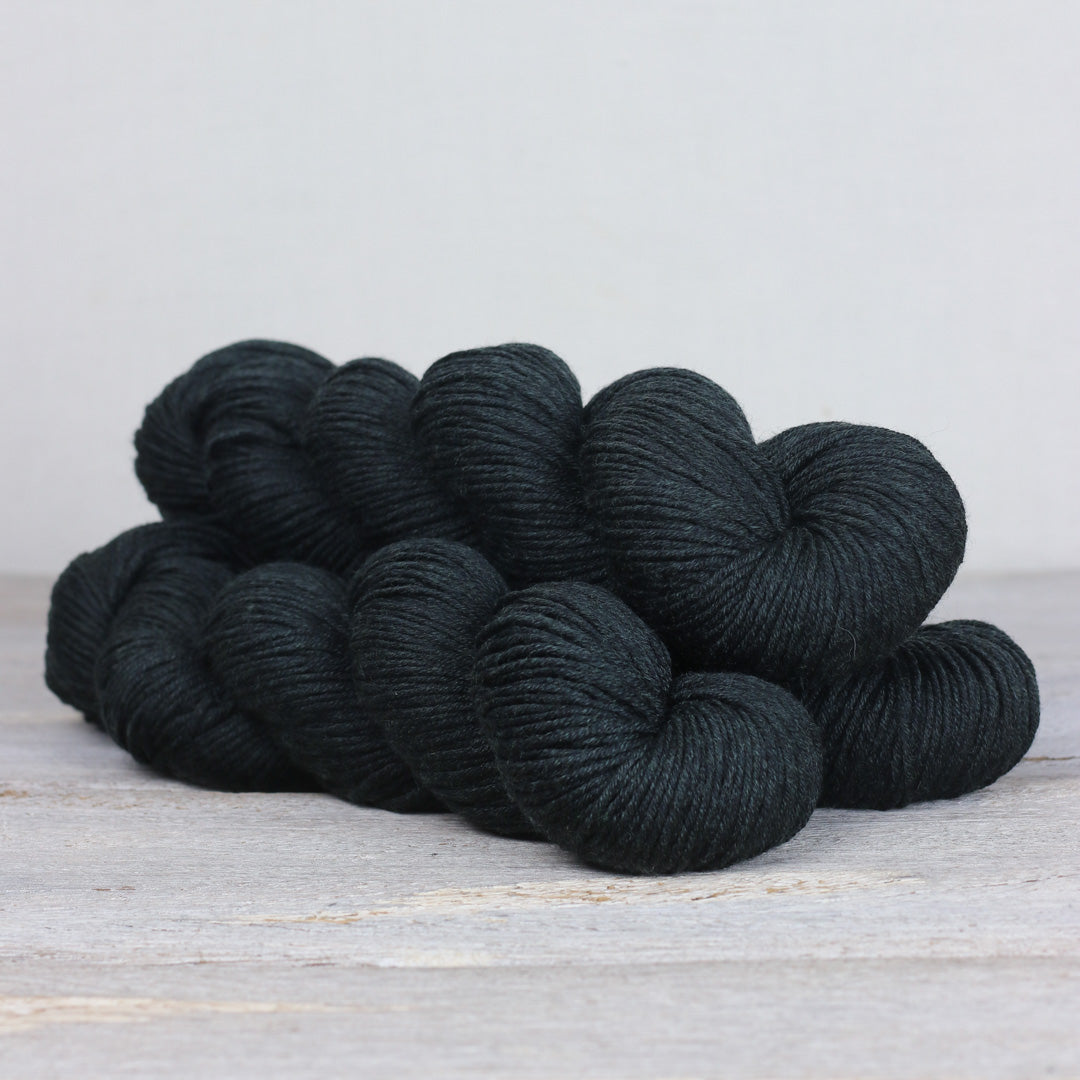 Skein of The Fibre Co. Herb & Hue yarn for knitting in a rich black color, ideal for warm projects.
