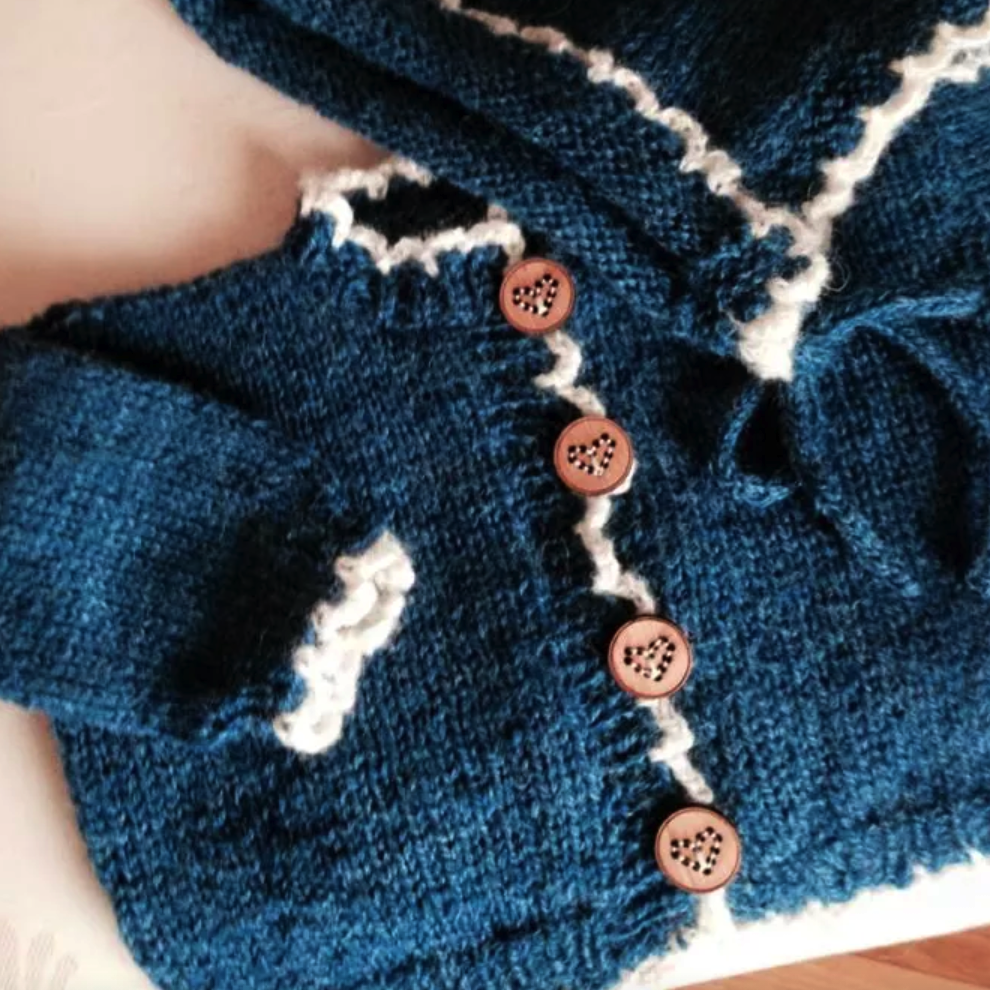 Hand-knit blue cardigan with heart buttons, featuring white trim and cozy design by Katrinkles