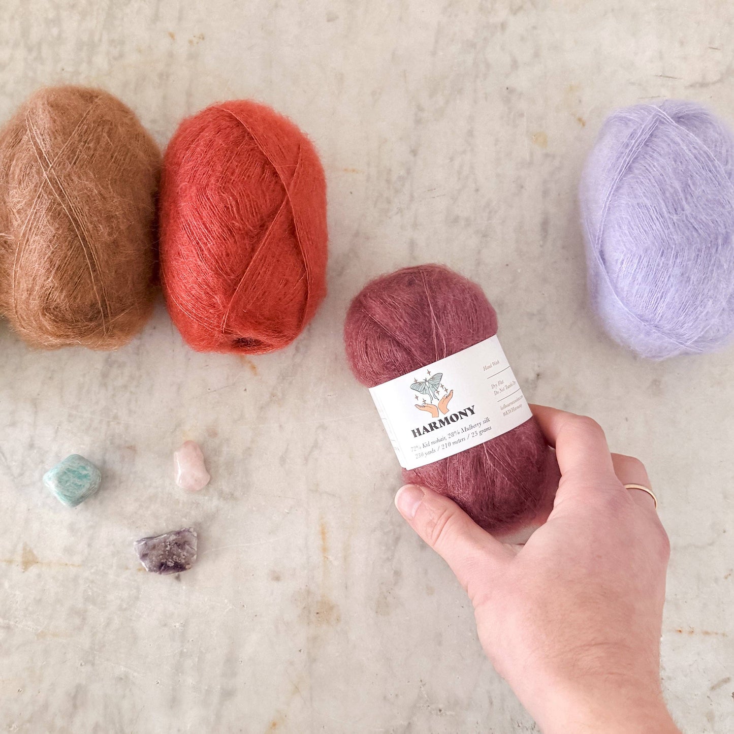 Various shades of Kelbourne Woolens Harmony yarn displayed with stones for crafting inspiration