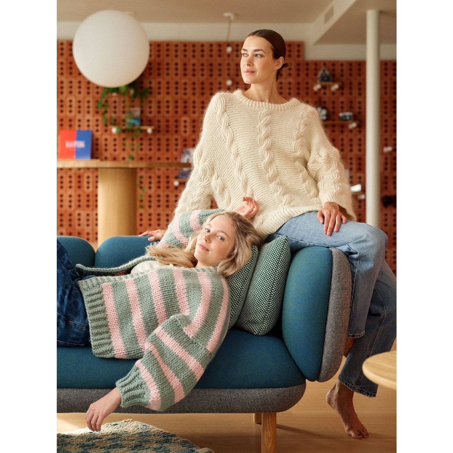 Two women modeling cozy sweaters showcasing unique patterns in knitting on a stylish couch