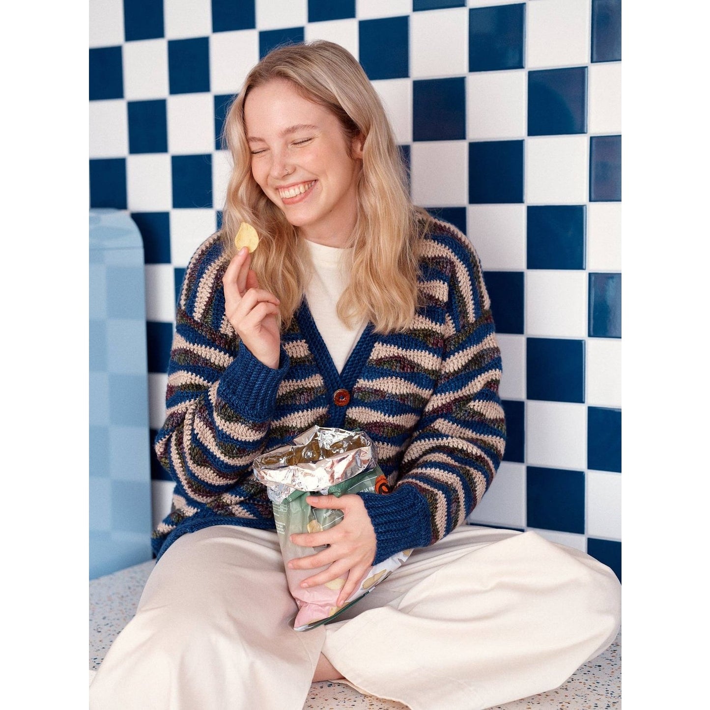 Woman smiling in striped cardigan, showcasing patterns in knitting on colorful background