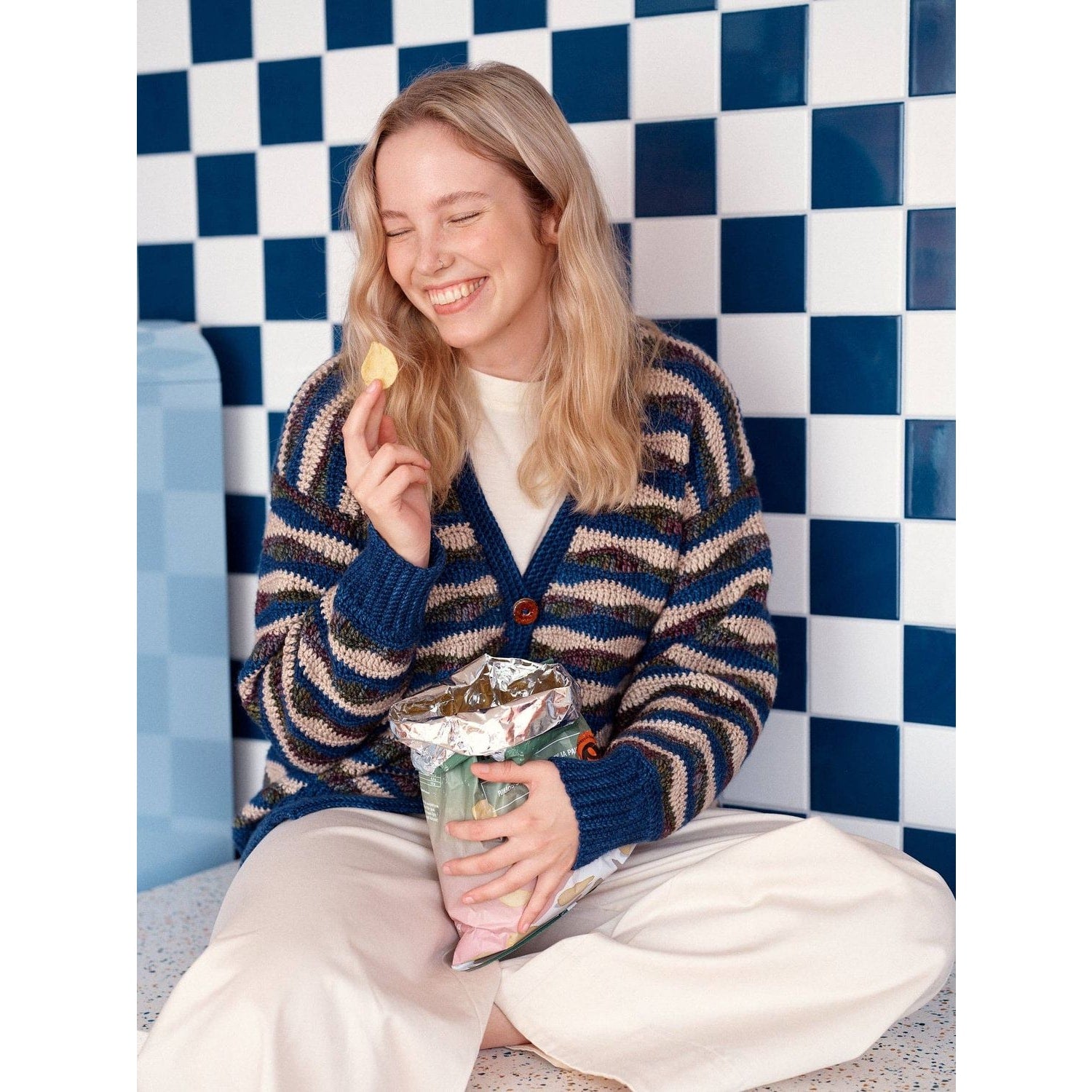 Woman smiling in striped cardigan, showcasing patterns in knitting on colorful background