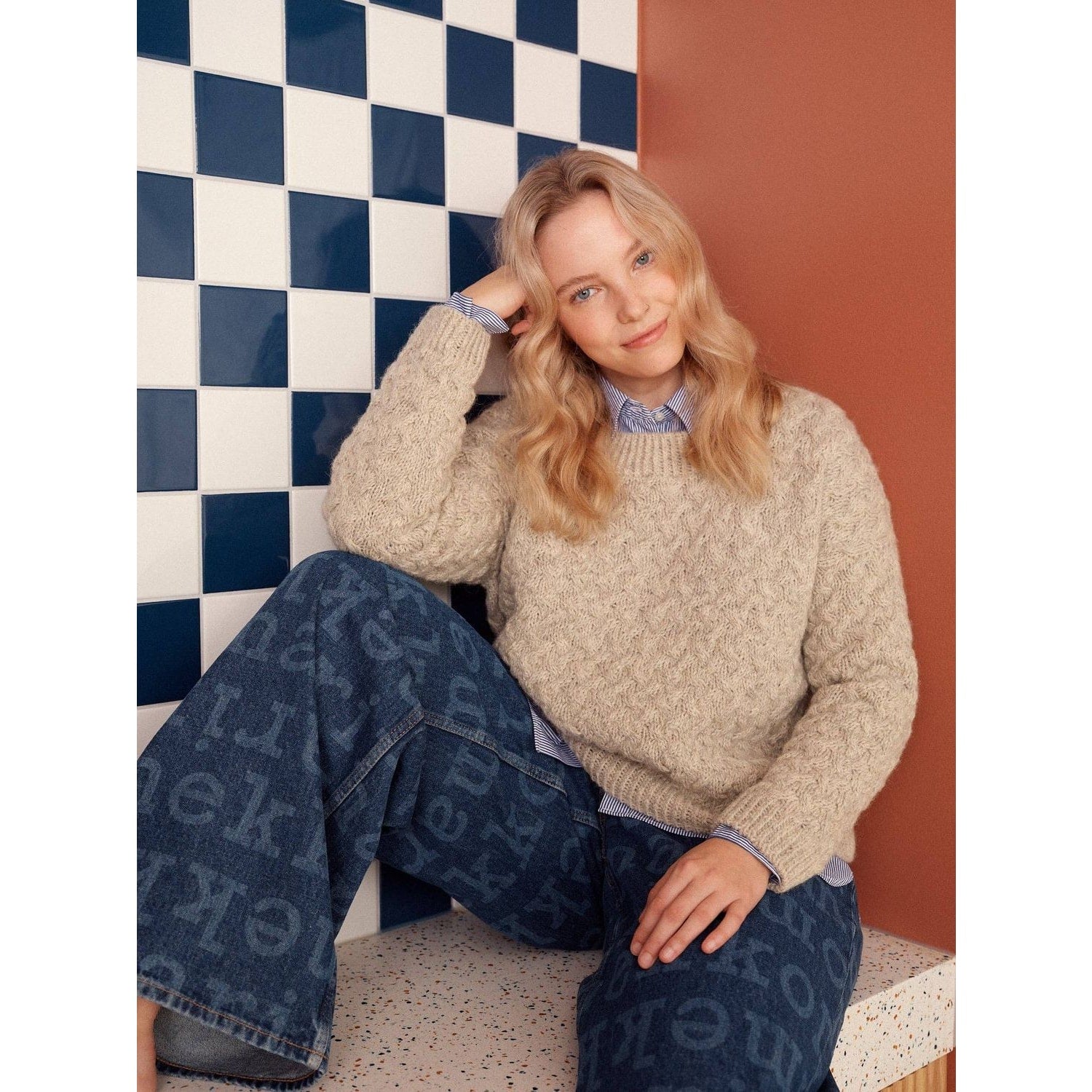 Woman wearing a cozy beige sweater made with unique patterns in knitting, styled with blue jeans