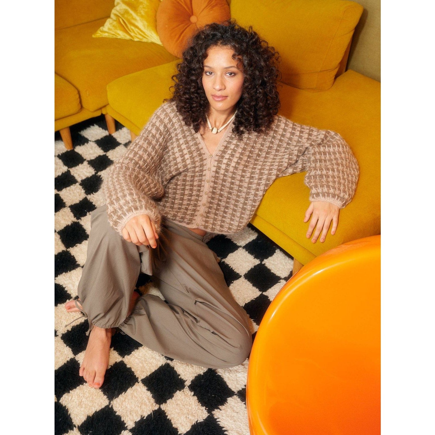 Cozy crochet with patterns sweater styled casually with relaxed pants on a colorful sofa