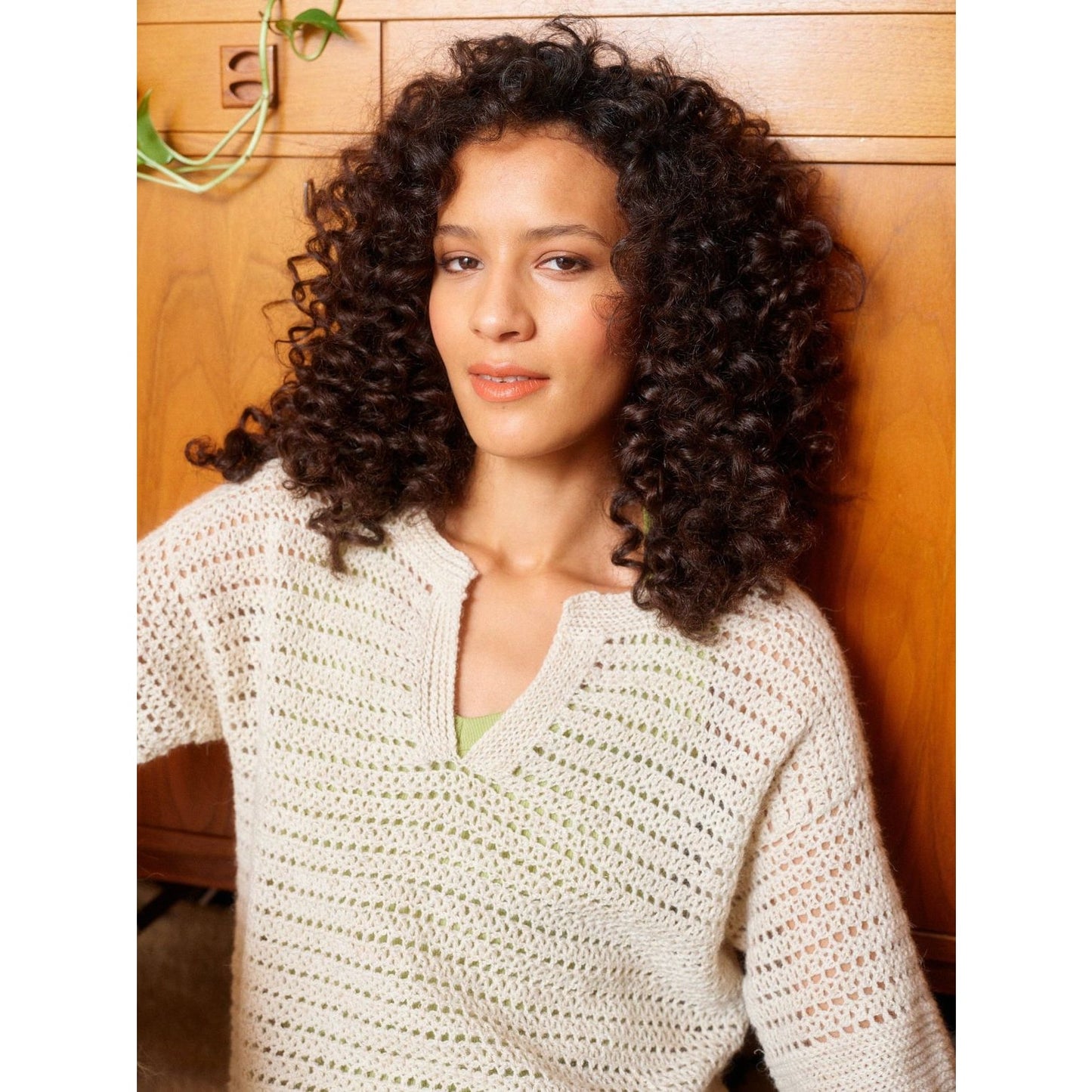 Woman modeling a cozy crochet sweater with patterns in a warm indoor setting