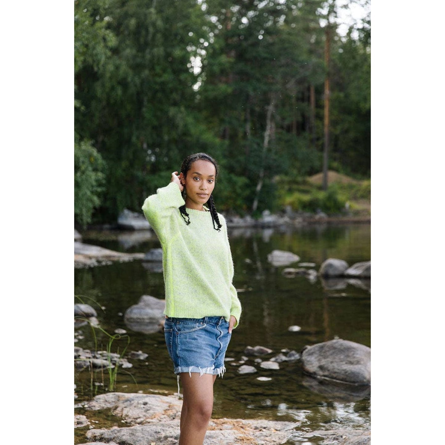 Model wearing a bright green sweater and denim skirt near a lake for Laine Magazine Issue 25