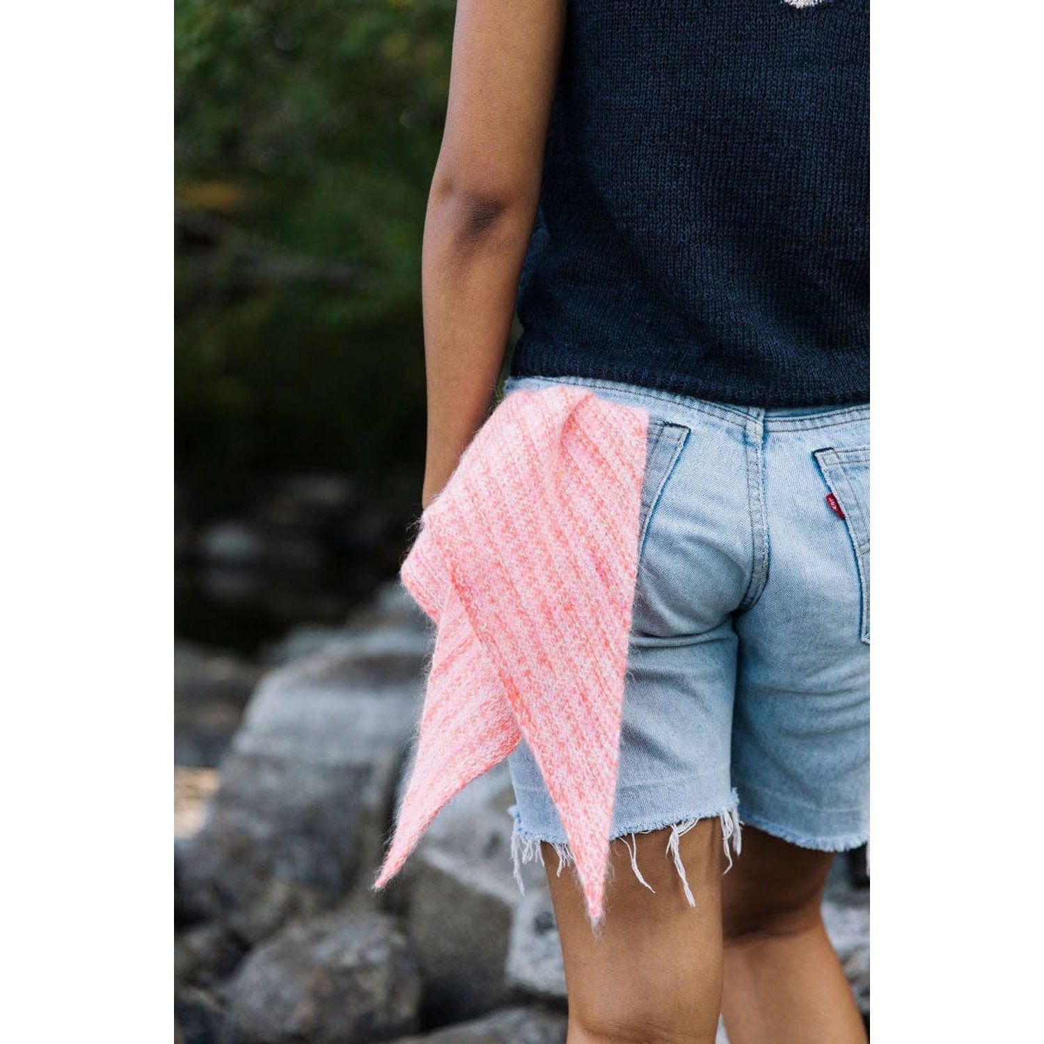 Person wearing a black top and denim shorts with a pink knit accessory from Laine Magazine Issue 25