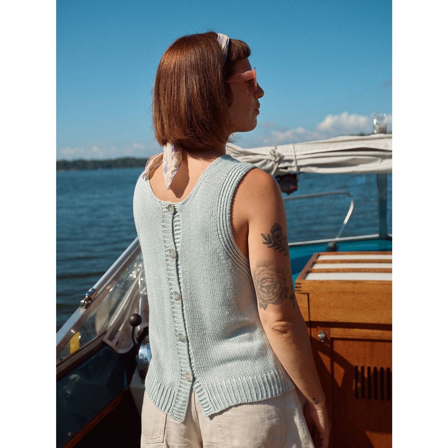 Model wearing a light blue knitted vest with back buttons, showcasing Laine magazine style at a boat by the water