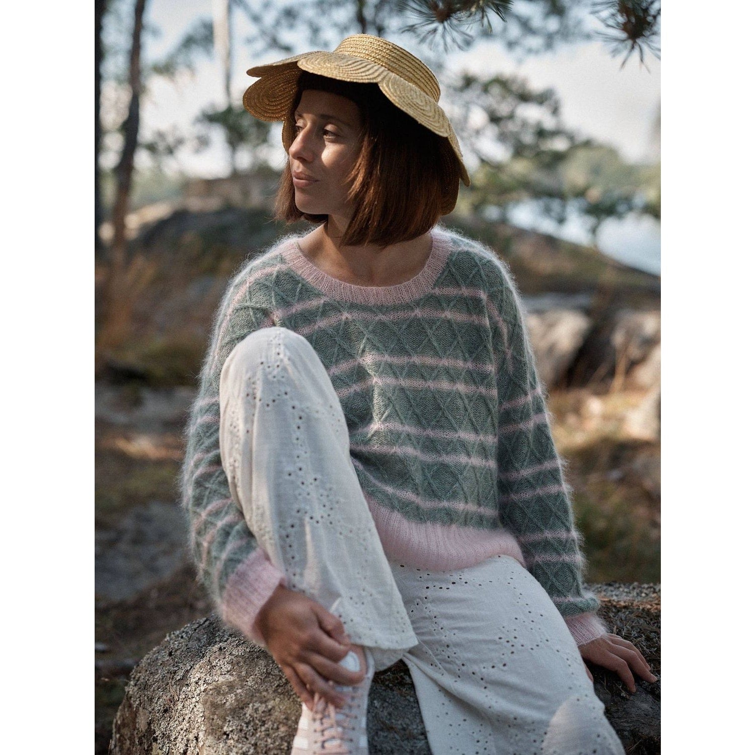 Model wearing a cozy knitted sweater from Laine Magazine with a straw hat in a natural setting