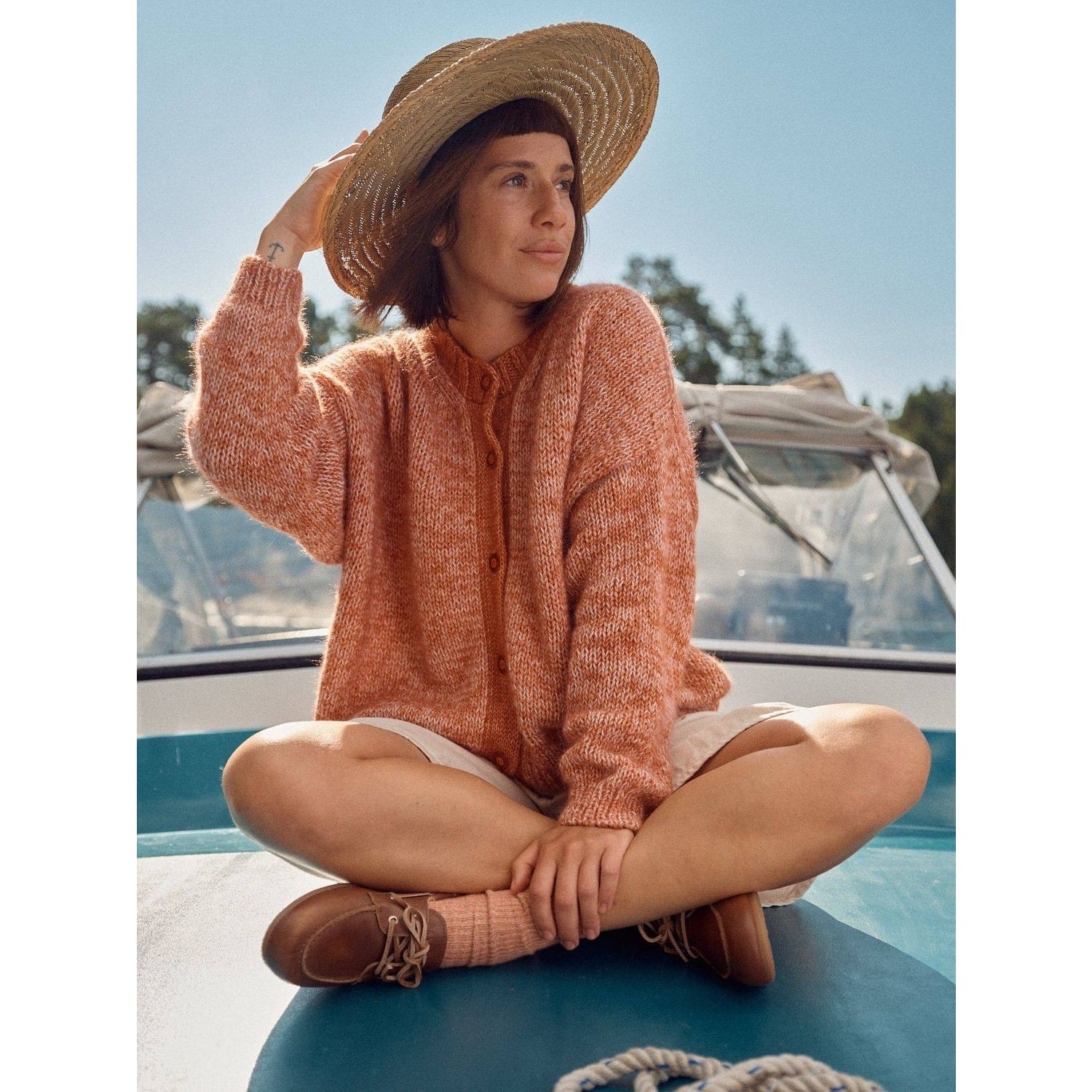 Woman in a cozy Laine magazine cardigan sitting on a boat wearing a wide-brimmed hat