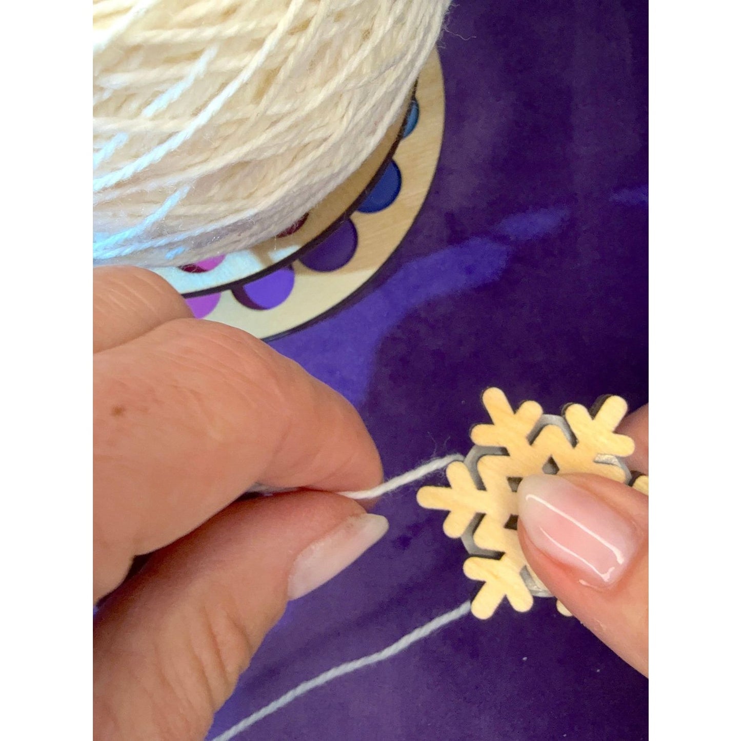 Hands crafting with Lemonwood elementary snowflake decorations and white yarn on a colorful craft surface