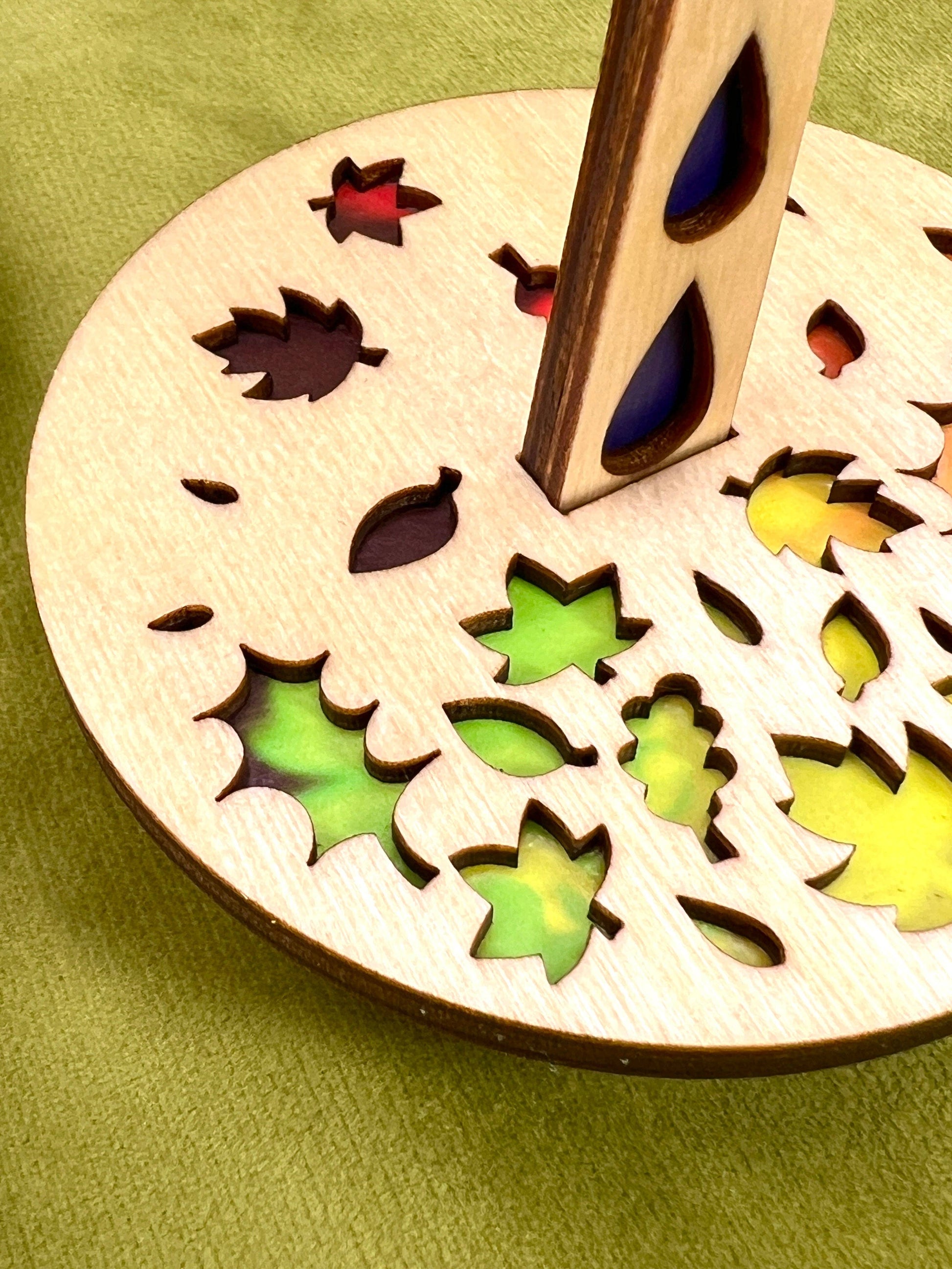 Lemonwood Autumn Tour stitch marker wooden disk with leaf cutouts and multicolor resin insets on green cloth