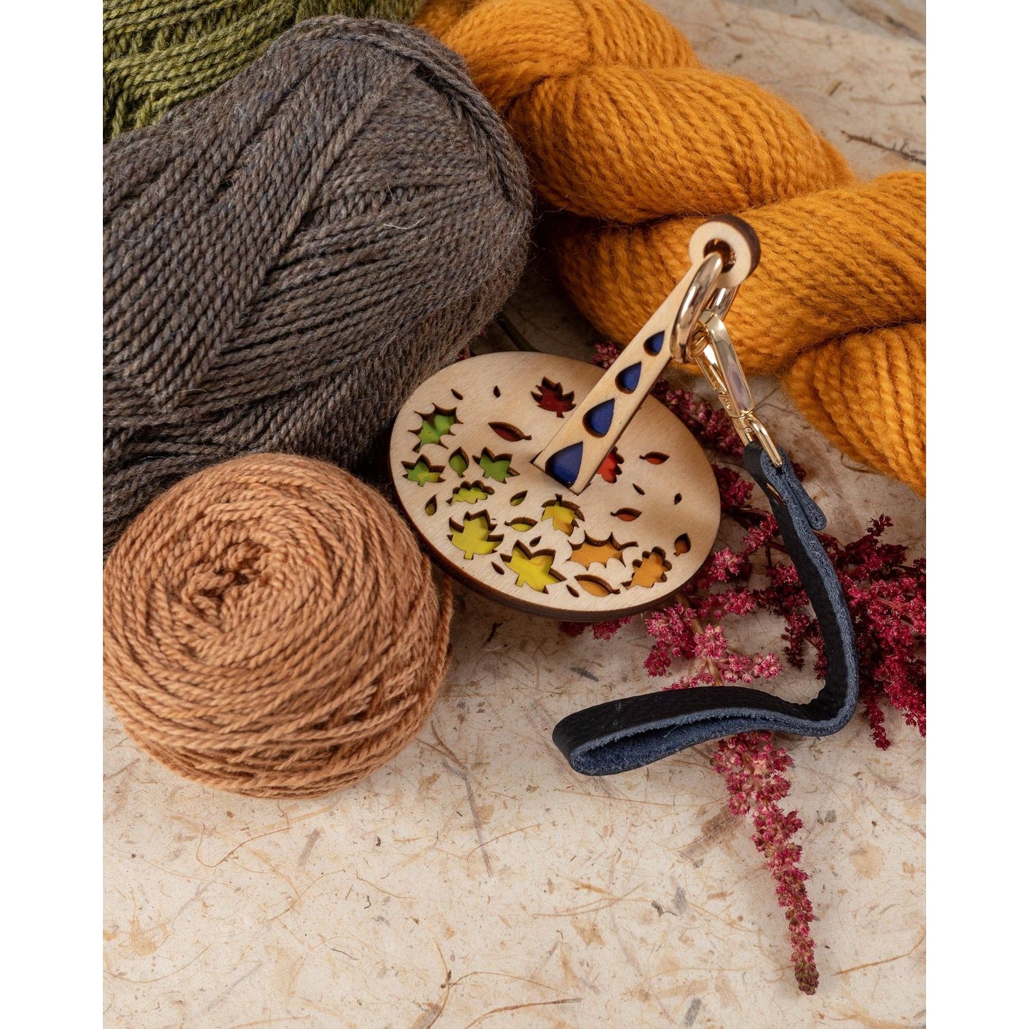 Lemonwood Autumn Tour stitch marker wooden key fob with leaf cutouts and leather strap beside mustard yellow gray and tan ya…