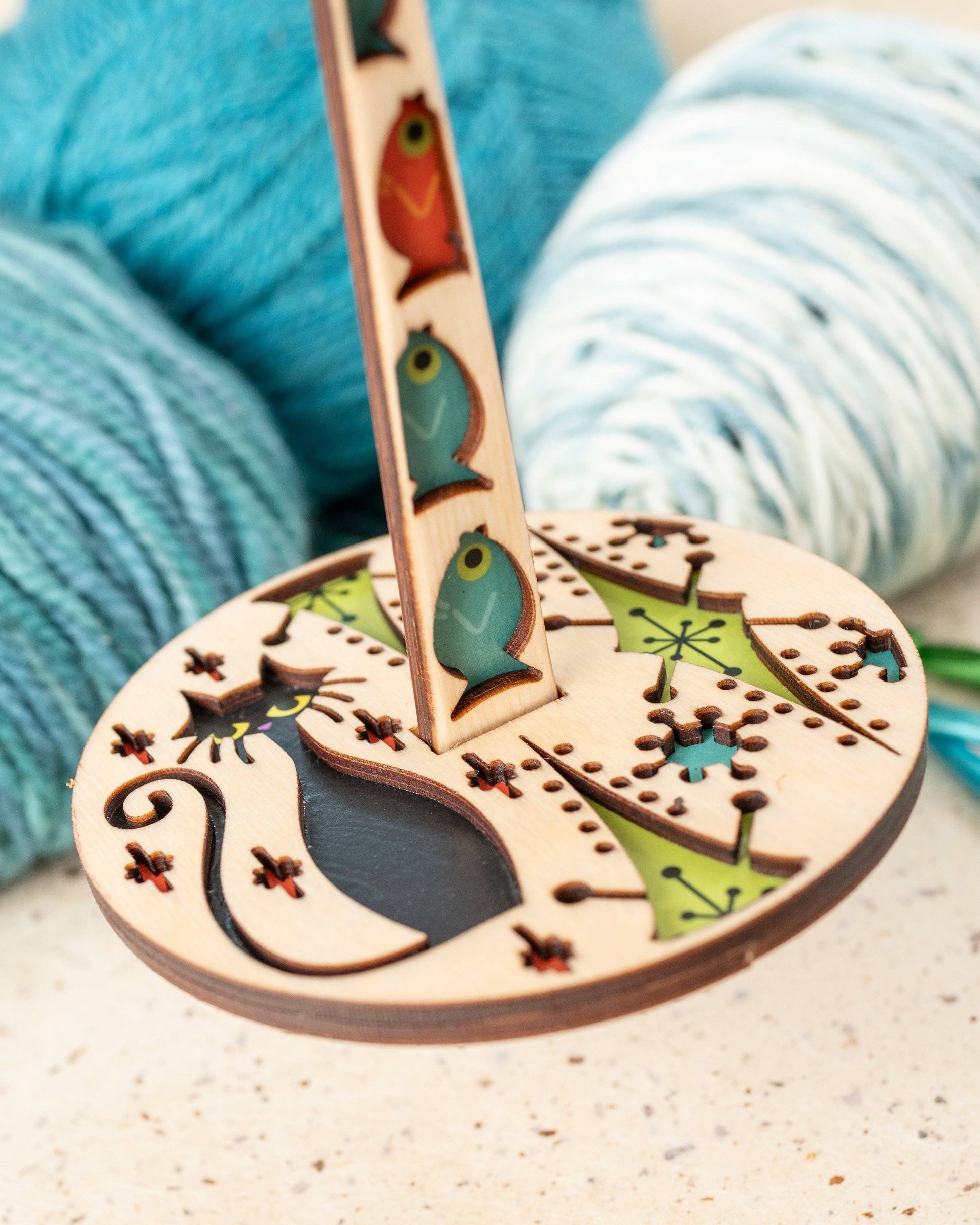 Wooden Lemonwood yarn holder with cat silhouette and fish motifs beside blue yarn balls lemonwood kitty kitty yarn accessory