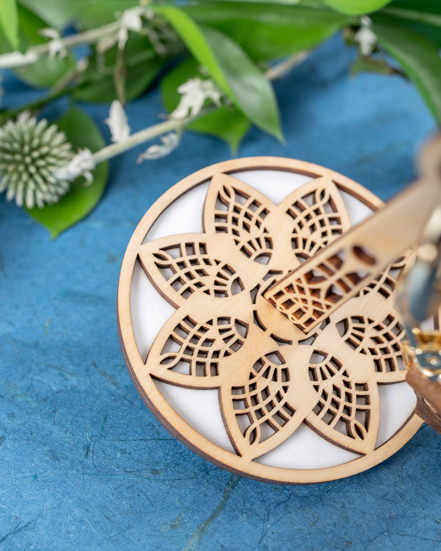 Laser cut wooden mandala thread holder pendant on blue cloth with greenery lemonwood crochet notions accessory