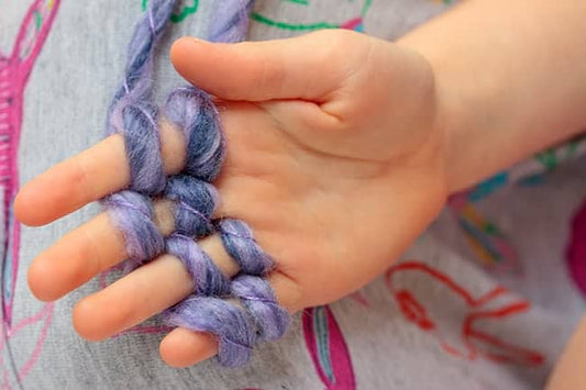 Small hands weaving chunky purple yarn loops on fingers during kids knitting workshop near Chicago at AriYARN Shop and Studio