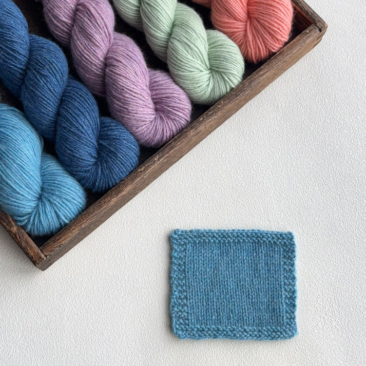 Lotus Yarns DK yarn in various colors displayed in a wooden box with a knitted swatch