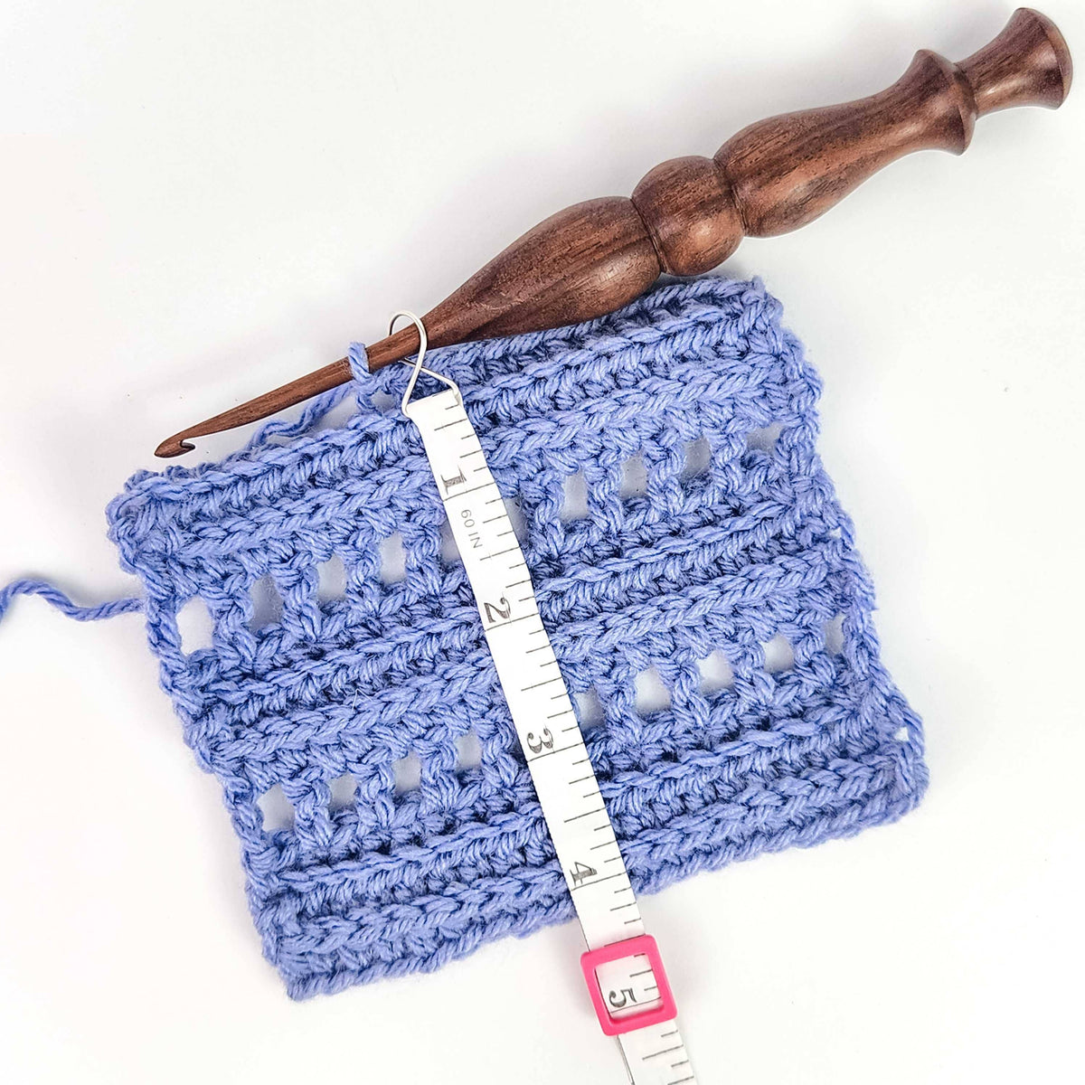 Crocheted blue swatch with a wooden crochet hook and measuring with tape for accurate sizing