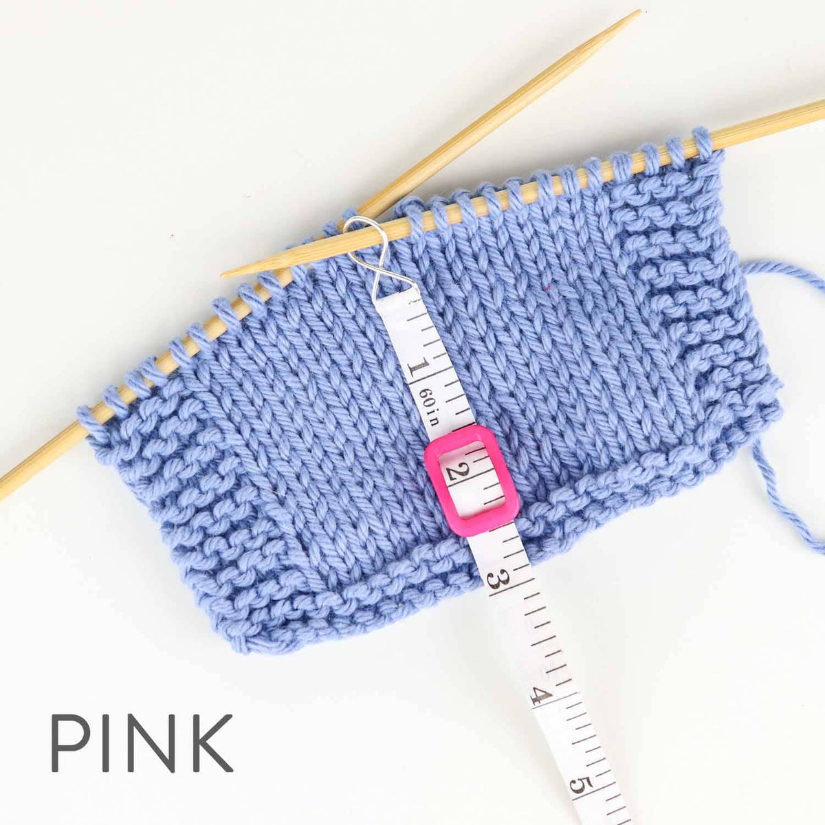 Knitted blue swatch on needles with a pink measuring tape showing precise measurements for knitting projects
