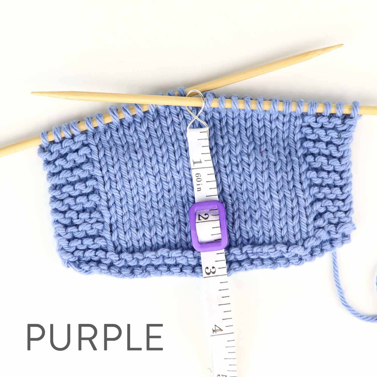 Knitted blue swatch with knitting needles and measuring with tape for accurate size measurement