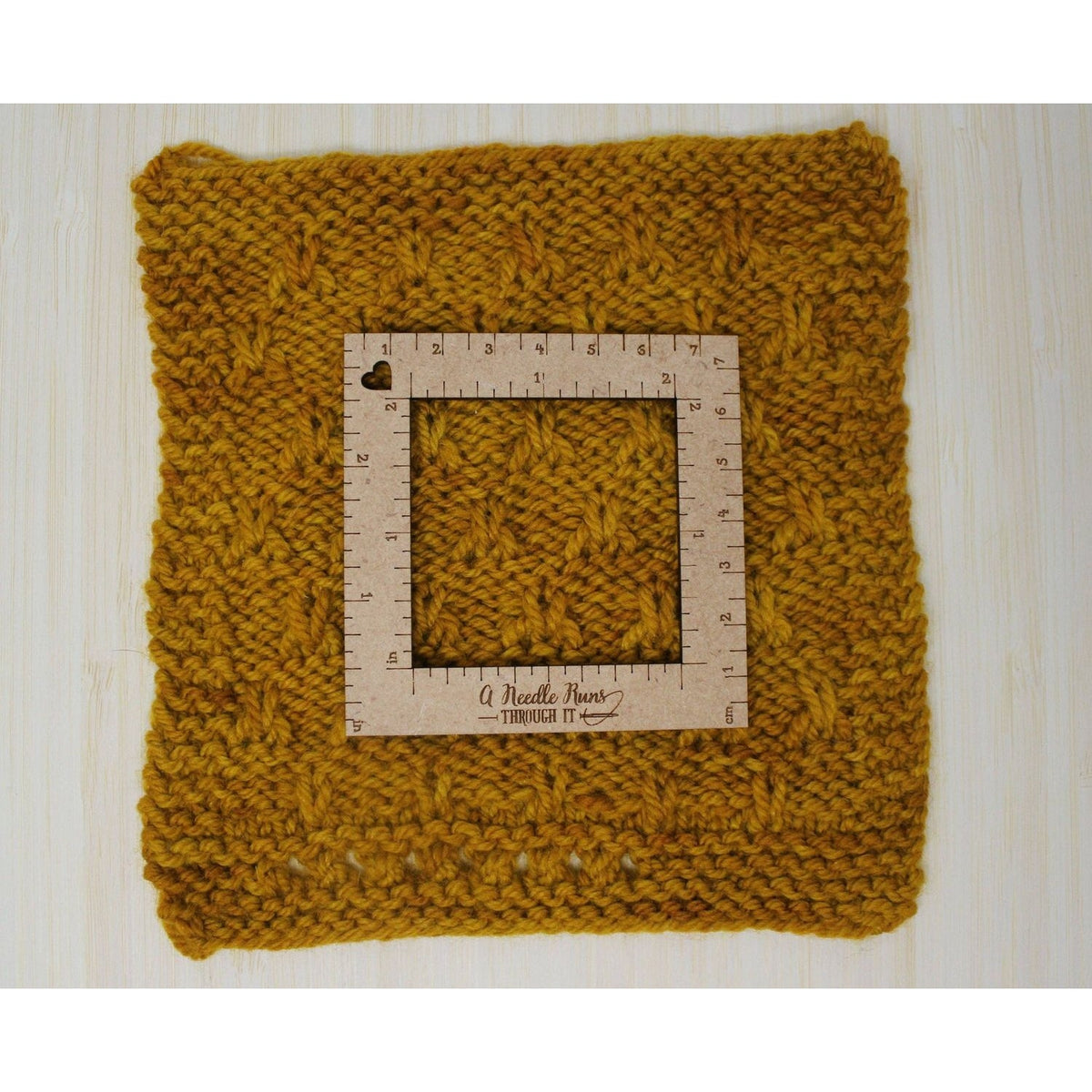 Knitting a gauge swatch displayed on a textured yellow knitted fabric with a measurement square