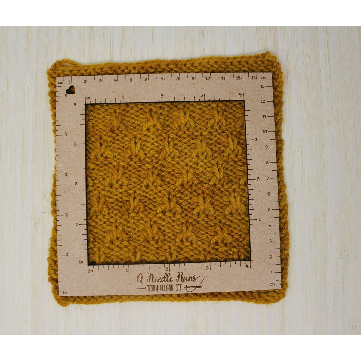 Knitting a gauge swatch displayed on a measurement ruler by A Needle Runs Through It