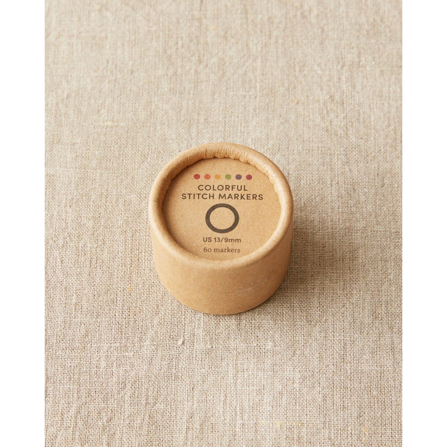 Original stitch markers for knitting by Cocoknits in a round cardboard container with colorful markers