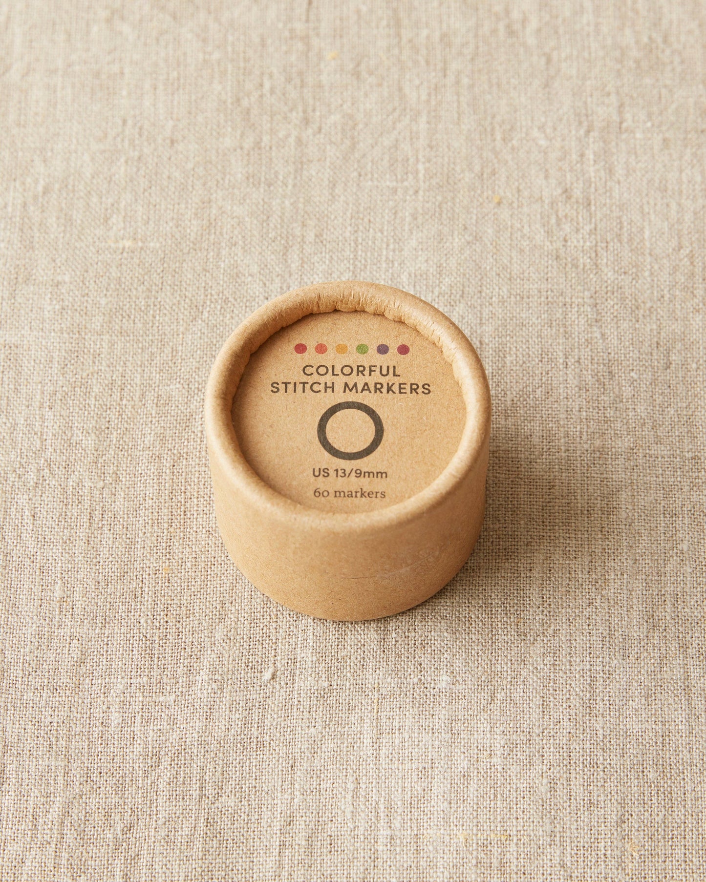 Original stitch markers for knitting by Cocoknits in a round cardboard container with colorful markers