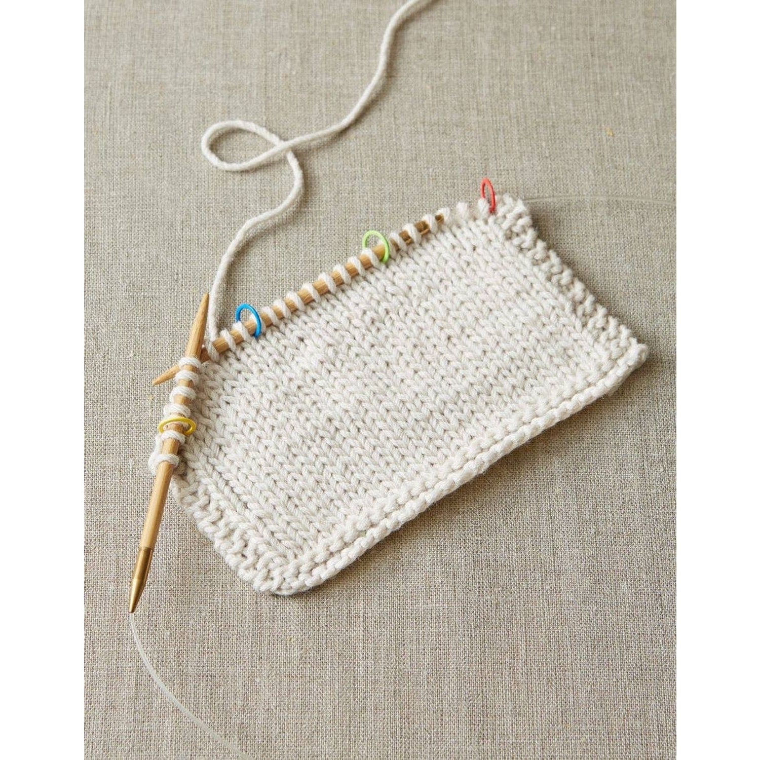 Knitting project with wooden needles and colorful original stitch markers for knitting on beige fabric