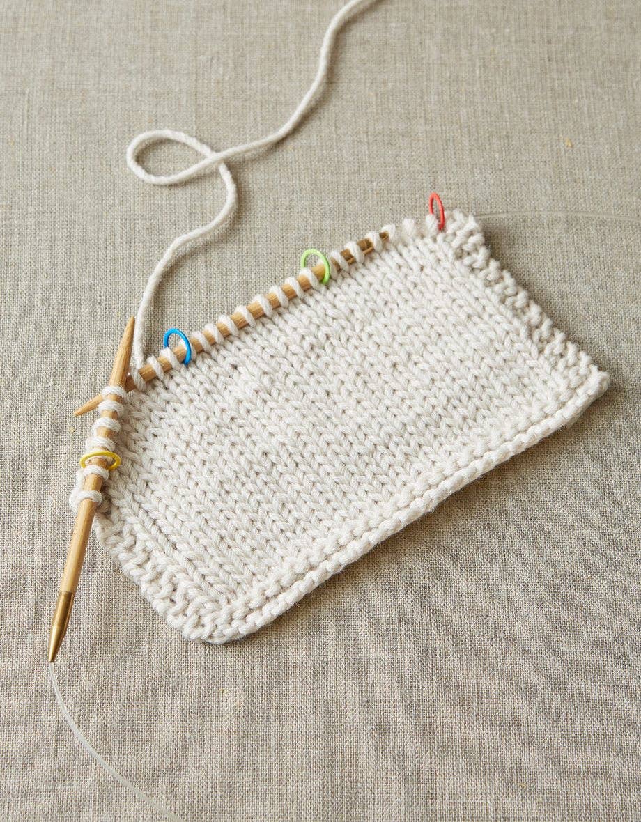 Knitting project with wooden needles and colorful original stitch markers for knitting on beige fabric