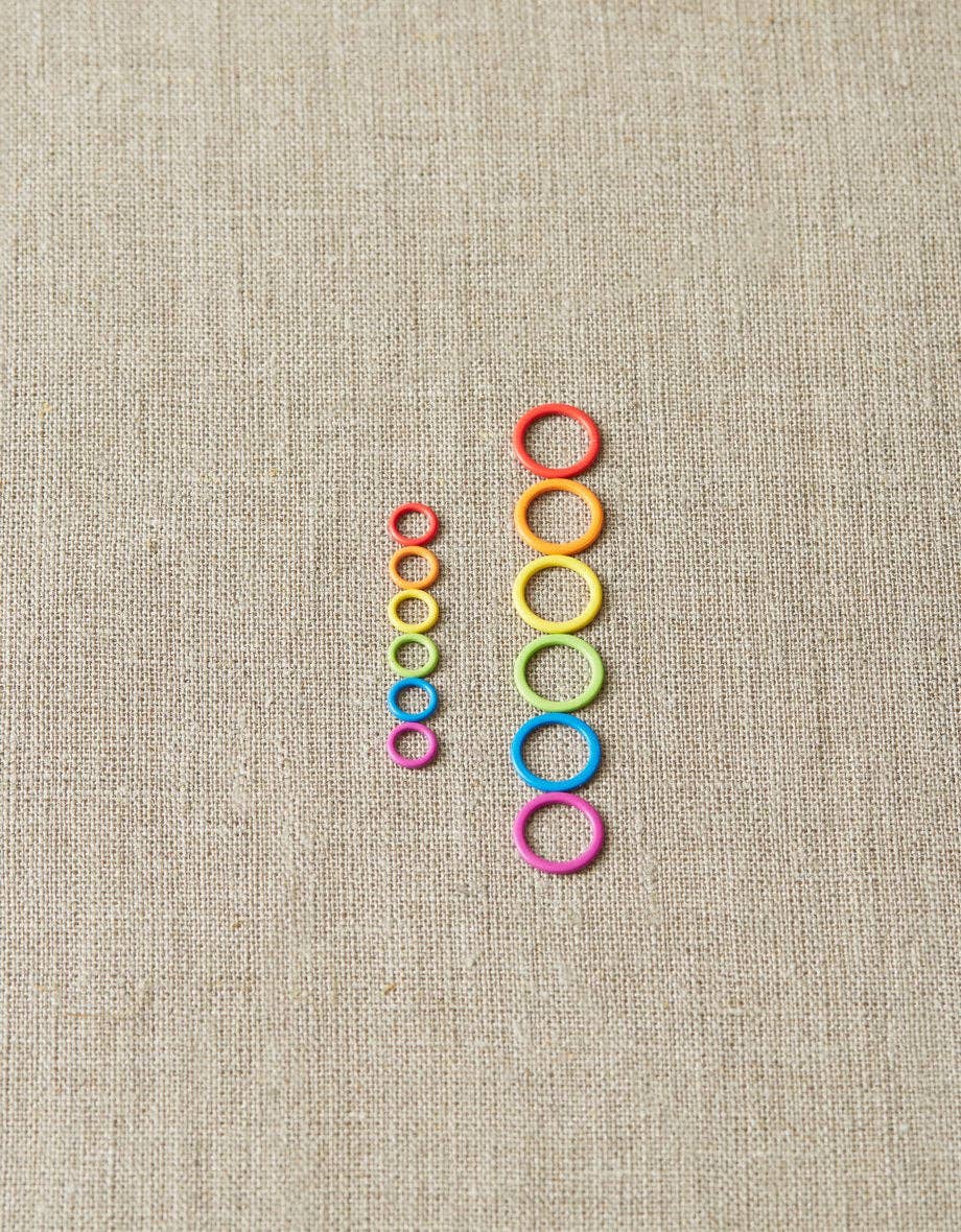 Cocoknits original stitch markers for knitting in a set of colorful rings arranged by size on beige fabric